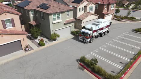 Garbage-truck-emptying-trash-can-in-front-of-house,-aerial-orbit-view