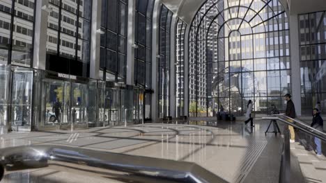 Sunlight-illuminates-Chicago's-modern-lobby-featuring-sweeping-glass-architecture-and-bustling-pedestrians,-pan-and-tilt-shot