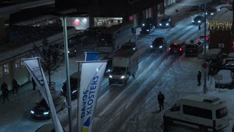 Eine-Nachtaufnahme-Aus-Der-Vogelperspektive-Zeigt-Den-Verkehr,-Der-Davos-Während-Des-Weltwirtschaftsforums-Verlässt.-Davos-Klosters-Banner-Sind-Sichtbar-Und-Menschen-Gehen-Durch-Die-Straßen