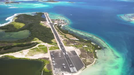 A-small-plane-landing-on-los-roques-archipelago-airstrip,-turquoise-sea,-aerial-view