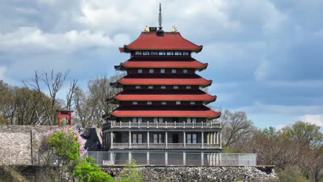 Red-multi-tiered-pagoda-with-traditional-East-Asian-architecture,-set-against-lush-trees-and-a-cloudy-sky