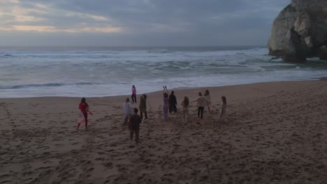 Grupo-De-Gente-Feliz-Bailando-En-La-Playa-De-Arena-En-Portugal-Después-Del-Atardecer