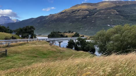 Man-runs-across-bridge-on-a-windy-day,-with-mountains-and-blue-sky,-New-Zealand