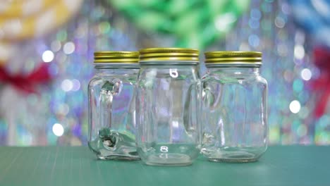 Three-empty-glass-jars-in-close-up-on-table-with-shiny-festive-background