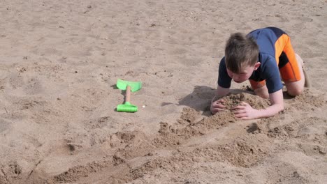 Kleiner-Junge-Im-Neoprenanzug-Am-Strand,-Der-Im-Sand-Gräbt