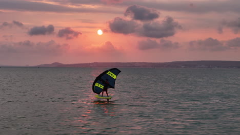 Surfer-Wing-Foiling-Under-A-Pink-Sunset-Sky-In-Mui-Ne,-Vietnam