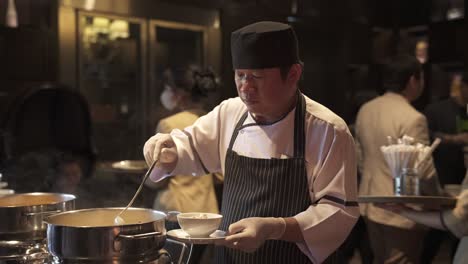 Chef-attentively-tasting-soup-in-a-bustling-restaurant-kitchen,-serving-with-precision