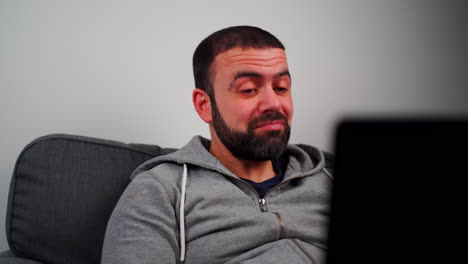 Middle-Eastern-Man-Sitting-On-Couch,-Smiling-And-Nodding-While-Using-Laptop