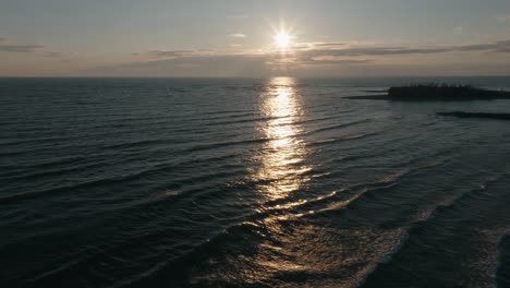 Sunset-over-calm-waters-near-Owen-Sound,-Ontario-with-light-reflecting-off-waves,-aerial-view