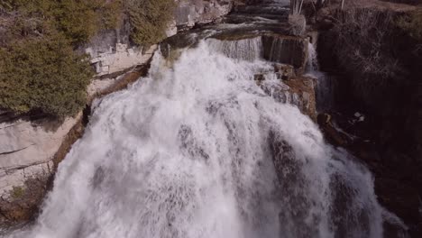 Rushing-waterfall-at-Owen-Sound-with-lush-surroundings-in-bright-daylight,-aerial-view