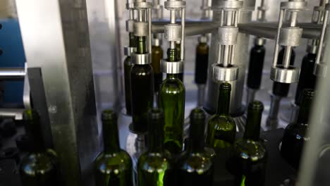 Wine-green-glass-bottles-filling-up-with-red-wine-at-an-automated-production-line-in-Vignonet-France,-Pan-left-medium-shot
