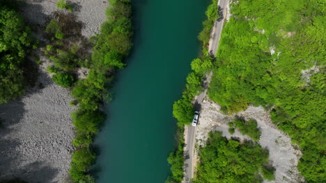 Bird's-eye-view-of-a-green-river-cutting-through-a-thick-forest,-showcasing-the-vibrant-colors-of-early-spring