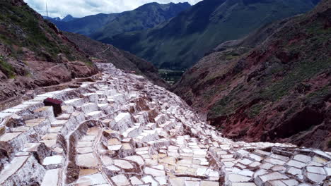 Salt-Mines-of-Maras-in-the-Sacred-Valley-of-Peru,-aerial-pullback-above-valley