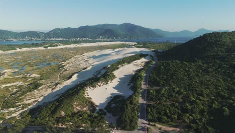 A-glimpse-of-the-sand-dunes-of-Joaquina-in-Florianopolis,-with-the-famous-Lagoa-da-Conceição-in-the-background