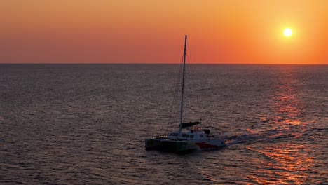 Low-tracking-aerial-follows-catamaran-driving-across-open-caribbean-waters-at-orange-sunset