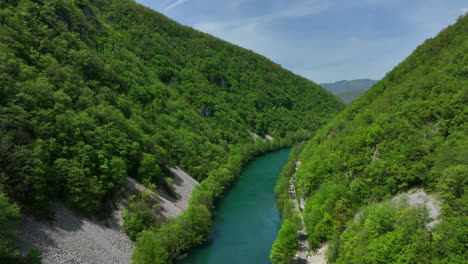 A-tranquil-river-surrounded-by-new-greenery-under-a-blue-sky-with-a-few-clouds,-viewed-from-a-low-flying-perspective