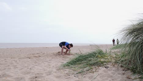 Young-boy-in-a-wetsuit-on-a-beach-digging-in-the-sand
