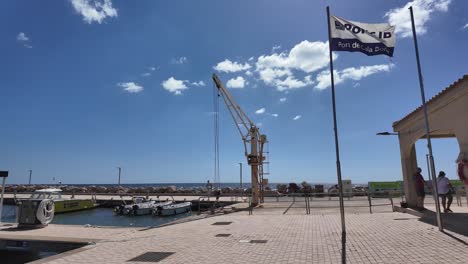 Puerto-Antiguo-De-Cala-Bona-Con-Una-Pareja-Caminando,-Red-De-Pesca,-Vista-Panorámica,-Hoteles-Tradicionales-Y-Pequeños-Barcos-De-Pesca,-Mallorca,-España