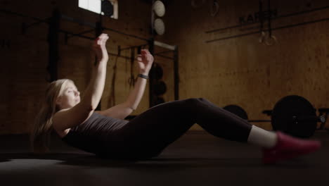 Low-angle-slomo-of-blonde-female-in-gym-doing-full-body-sit-ups,-abs-workout