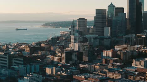 Una-Vista-Aérea-Dinámica-Del-Horizonte-De-Seattle-Y-Del-Centro-Urbano-Junto-A-Puget-Sound-Y-Un-Horizonte-Brumoso