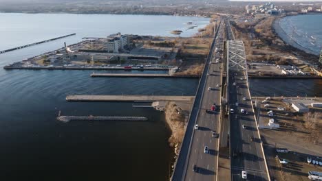 The-skyway-bridge-over-calm-waters-in-hamilton,-ontario-at-dusk,-cars-in-motion,-aerial-view