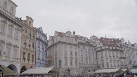 Crowded-Old-Town-Square-in-Prague,-bustling-with-diverse-tourists-on-an-overcast-day,-tilt-down-shot