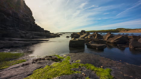 Time-lapse-of-rising-coastal-tide-on-a-sunny-cloudy-day-on-Streedagh-cliff-beach-with-sea-algae-and-rocks-in-the-foreground-in-county-Sligo-along-Wild-Atlantic-Way-in-Ireland
