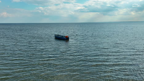 Un-Pequeño-Barco-Flota-Suavemente-En-Aguas-Tranquilas-Del-Mar,-Amarrado-Solo-Bajo-Un-Vasto-Cielo-Abierto