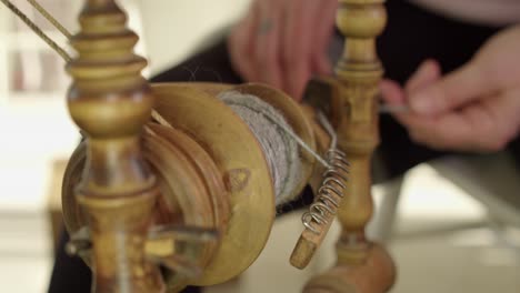 Spinning-wheel-bobbin-foreground,-defocused-artisan-hands-background