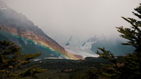 Hike-Argentina,-View-of-El-Chalten,-Cerro-Torre-Through-Trees,-Beautiful-Snow-Capped-Mountain-Range,-Rainbow,-Misty,-Establishing-Shot