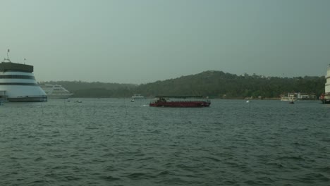 Large-cruise-ship-and-smaller-boats-on-a-hazy-river-with-a-lush-hillside-backdrop-in-India