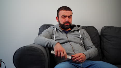 Man-Turns-On-The-Television-With-Remote-Control-While-Sitting-On-The-Sofa