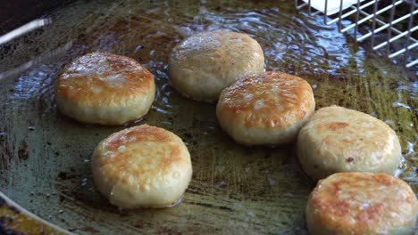 Freshly-made-Chinese-meat-pie-cooking-and-sizzling-on-hot-oil-pan,-a-stall-vendor-flipping-the-pie-pastry-using-kitchen-tongs,-pan-frying-until-golden-brown,-close-up-shot-of-popular-Asian-food