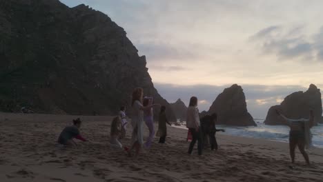 Glückliche-Frauen-Tanzen-Auf-Sand-Vor-Dem-Meer-Mit-Großen-Klippen-Im-Hintergrund