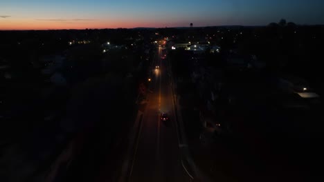 Drone-flyover-dark-street-with-traffic-after-sunset-time-in-american-town