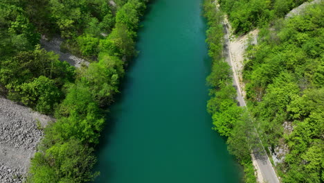 Aerial-view-of-a-vibrant-green-river-meandering-through-a-dense-forest,-with-early-spring-foliage