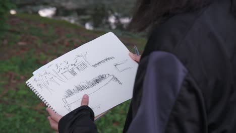 Rear-medium-shot-of-young-female-adult-picking-up-sketchbook-revealing-scary-drawing-in-outdoor-park