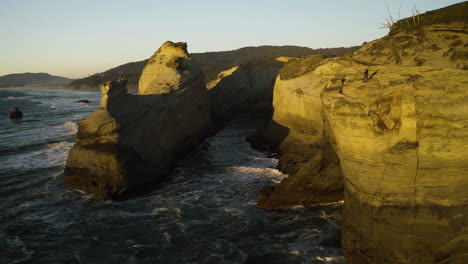 Slow-aerial-descend-following-waves-entering-sandstone-cove-in-Cape-Kiwanda,-Oregon-Coast