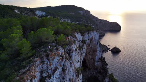 Hikers-rest-on-a-rocky-cliff-among-trees-with-a-view-of-the-green-landscape-during-sunset-in-ibiza