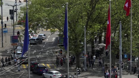 Right-panning-drone-shot-of-Zurich-city-centre-showing-cars-waiting-at-traffic-lights,-pedestrians,-the-Swiss-flag-and-people-sat-on-the-lake-front