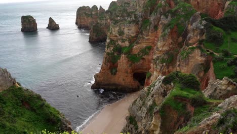 Die-Kamera-Schwenkt-Nach-Oben-Und-Zeigt-Die-Wunderschönen-Roten-Sandsteinfelsen-Und-Hoch-Aufragenden-Felsformationen-Entlang-Der-Küste-Der-Algarve-In-Der-Region-Lagos-Im-Süden-Portugals