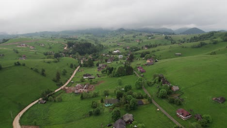 A-lush-green-village-nestled-among-rolling-hills-on-a-cloudy-day,-aerial-view