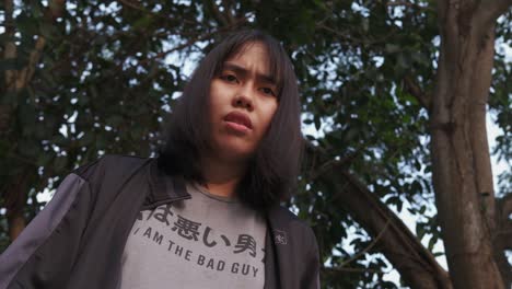 Front-view-of-young-Asian-girl-in-forest-park-approaching-camera-looking-ahead