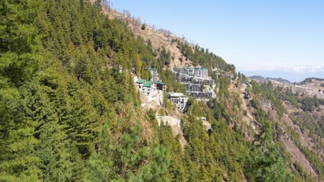 Hillside-buildings-nestled-among-dense-forests-on-a-steep-mountain-slope-under-a-clear-blue-sky