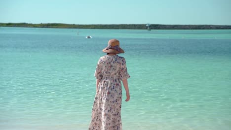 Frau-Mit-Hut-Und-Kleid-Dreht-Sich-Um-Und-Sieht-Ein-Wunderschönes-Meer,-Langsame-Rückaufnahme