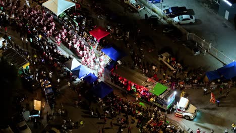 Shining-lights-illuminate-path-for-Carnaval-performers-in-parade-at-night,-aerial