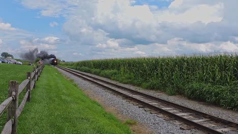 A-vintage-steam-train-powers-through-lush-rural-fields-under-a-serene,-cloud-dappled-sky