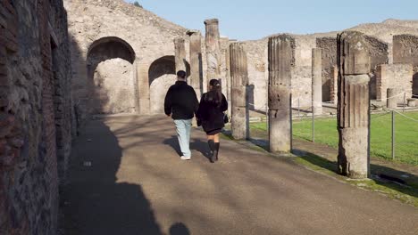Reisendes-Paar,-Das-An-Steinsäulen-In-Der-Gladiatorenkaserne-In-Pompeji,-Italien-Vorbeigeht