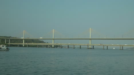Wide-shot-of-a-bridge-over-a-river-with-a-yacht-passing-underneath-in-daylight