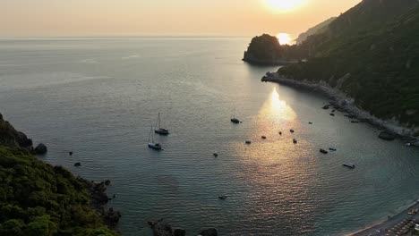 Sunset-view-over-a-serene-bay-in-Corfu,-Greece-with-boats-and-lush-greenery